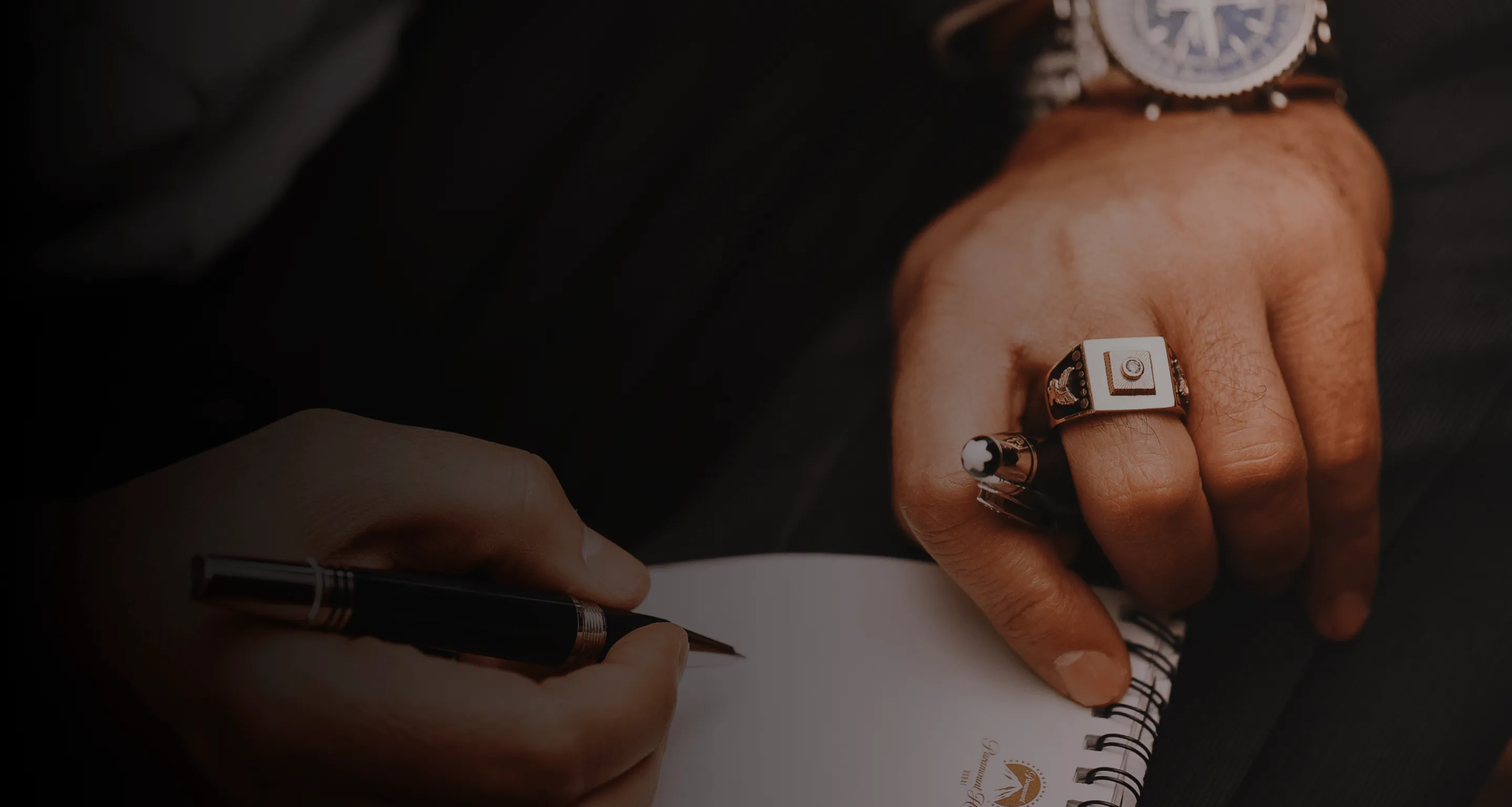 Man met horloge en ring schrijft in notitieboekje met pen.