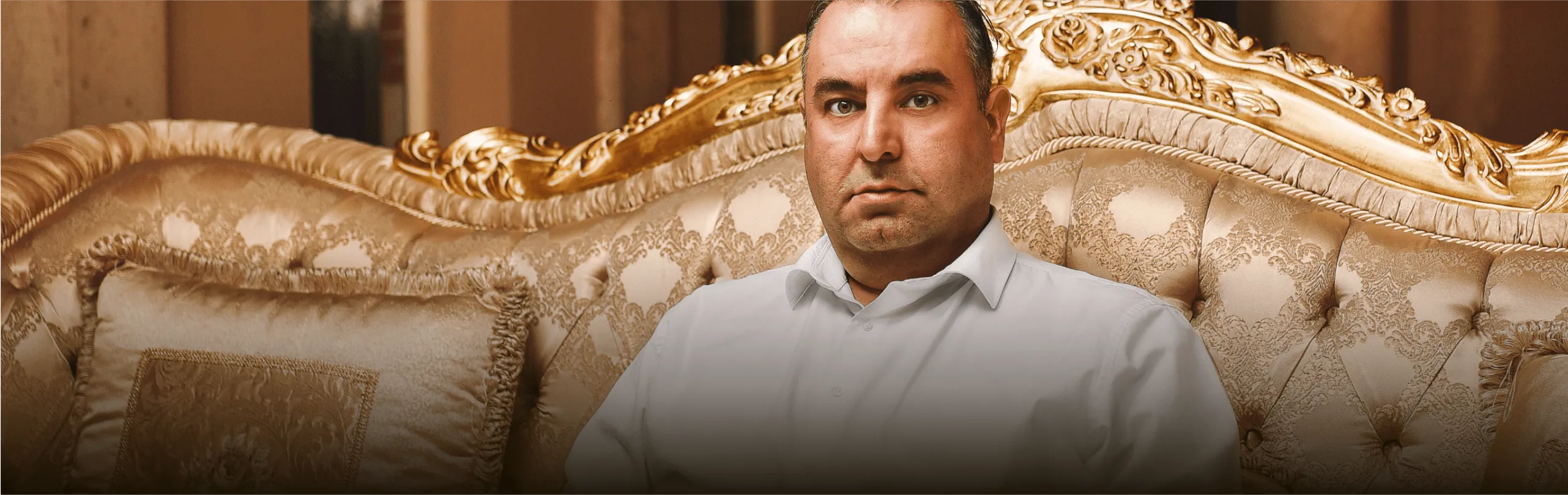 Man in wit overhemd zittend op luxe gouden bank.